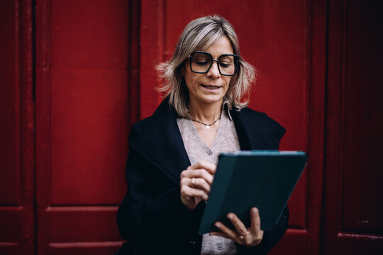 Professional woman focused on digital tablet screen standing outdoors, female executive managing remote business tasks, online banking and financial data analysis, modern tech lifestyle.