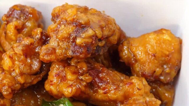 close-up stock shot of crispy, deep-fried chicken pieces tossed in a rich, glossy, and spicy dark Manchurian gravy sauce. The dish is garnished with fresh green chili peppers, showcasing a popular and