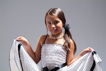 Charming young girl in a polka dot dress holding out her skirt with a sweet smile against a grey studio background © RRestrepo