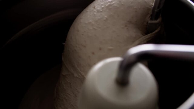 Whole wheat bread dough being kneaded in robust home stand mixer with rotating bowl, for wholemeal sourdough bread. Close-up, slow camera push in. 