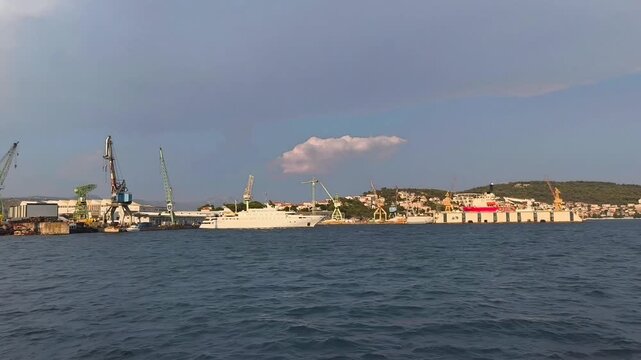 Trogir, Croatia - August 06, 2026: Coastal view of shipyard with cranes and boats, showcasing the vibrant harbor activity and scenic backdrop of the waterfront landscape