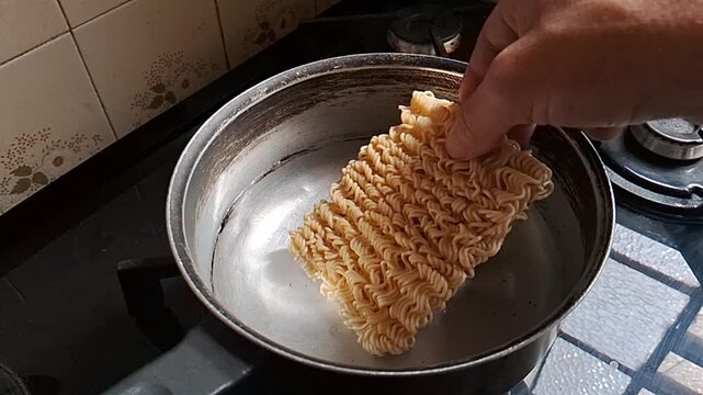 Hand placing dry instant noodle block into hot boiling water