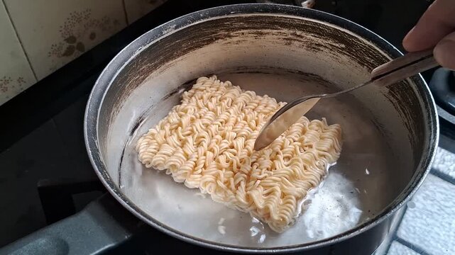 Dry instant noodle block boiling in hot metallic cooking pot