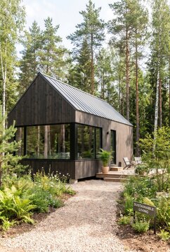 Modern wooden house with large windows surrounded by trees and greenery, featuring a pathway and a sign indicating sustainable living in a tranquil forest setting