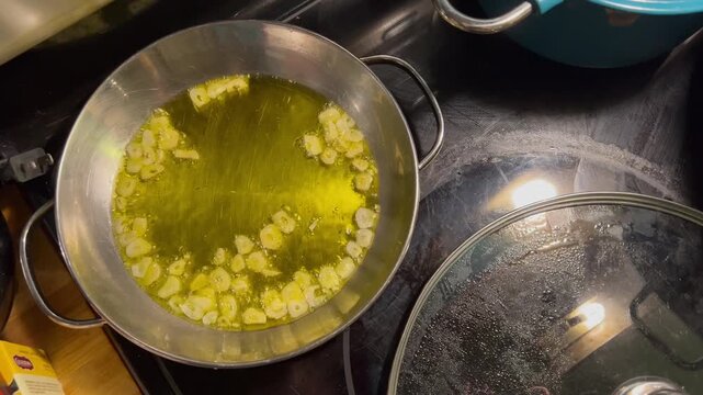 Sliced garlic sizzling in olive oil inside a stainless steel pan