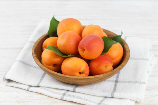 Fresh ripe apricots in rustic wooden bowl with green leaves on white wooden background. Healthy seasonal summer fruit, healthy food, natural nutrition, ingredient for cooking and desserts.
