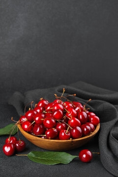 Fresh ripe sweet cherries in wooden bowl with green leaves on black textured background, copy space. Healthy organic summer fruit, juicy red berries, natural freshness, healthy eating, seasonal food