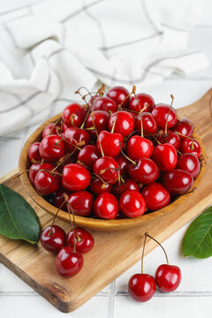 Fresh ripe red sweet cherries in wooden bowl with green leaves on light textured background. Healthy organic summer fruit, juicy red berries, natural freshness, healthy eating, seasonal food