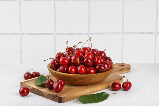 Fresh ripe red sweet cherries in wooden bowl with green leaves on white tiled textured background. Healthy organic summer fruit, juicy red berries, natural freshness, healthy eating, seasonal food