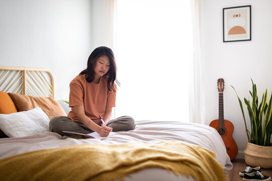 Young woman writing journal on bed at home