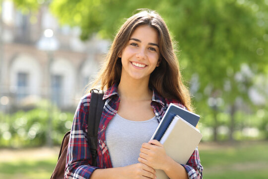 Happy teenage student holding notebooks outdoors at school, captured in warm sunlight with a candid smile and softly blurred campus background.