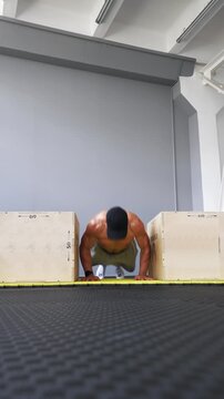 Muscular man performs a burpee between two plyo boxes indoors. Fitness, conditioning, endurance, strength and high-intensity training concepts. Vertical video.