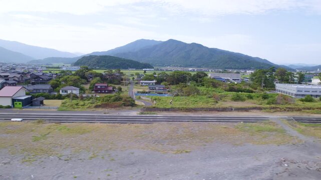 海辺の線路沿いの空き地と町並みを左へ横移動で撮影した空撮 / Drone tracking left of coastal town