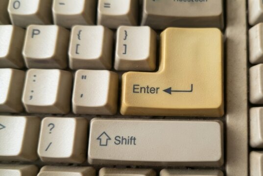A yellowed enter key stands out on a dirty retro computer keyboard from the nineties.