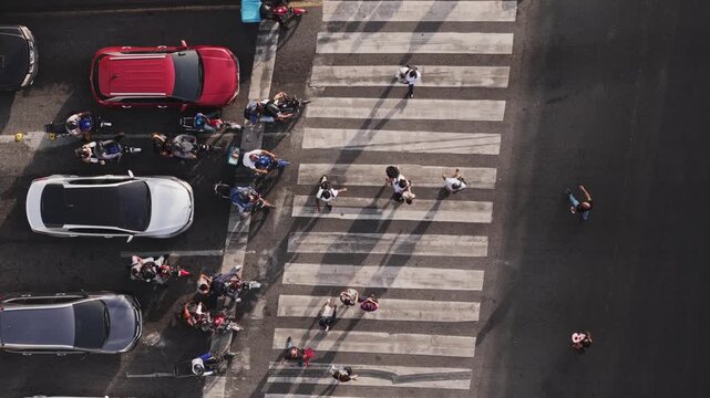 Directly overhead top-down view of cars and motorbikes stopped at a pedestrian zebra crossing