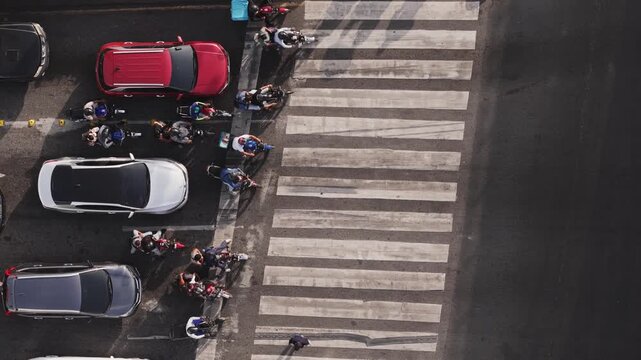 Drone view perspective of commuters and delivery riders waiting at a crosswalk during rush hour