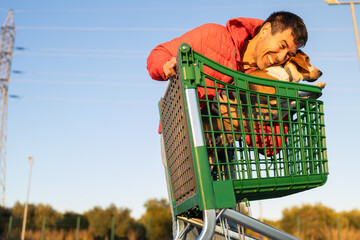 Man smiling and hugging his dog as they ride in a supermarket shopping cart at golden hour in warm sunset light © D.Petrus