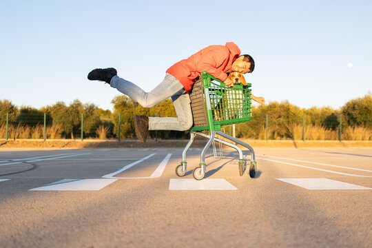 smiling man riding a shopping cart with his dog in an empty parking lot at sunset  with a warm sunlight during the golden hour