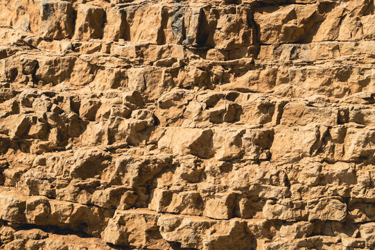 Layered sandstone rock texture with deep shadows and warm ochre tones