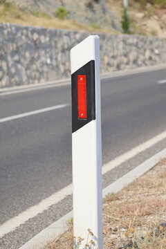White plastic road delineator post with red reflector on an asphalt highway in Croatia