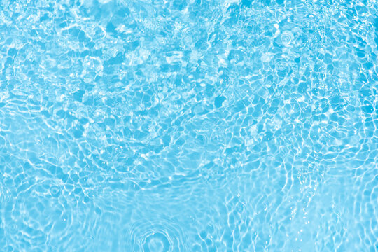 Blue water with ripples on the surface. Defocus blurred transparent white colored clear calm water surface texture with splashes and bubbles. Water waves with shining pattern texture background.