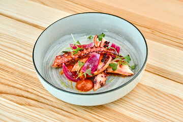 Grilled octopus dish served in a modern bowl on wooden table © Elizaveta