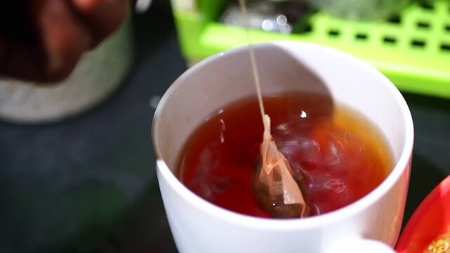 Person Steeping Tea Bag in Hot Tea in White Mug Close-up