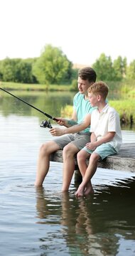 Father and his little son fishing together near river outdoors