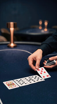 Hand dealing playing cards on a deep navy felt table. Close-up of dealer placing a seven of hearts card during a poker game in a casino