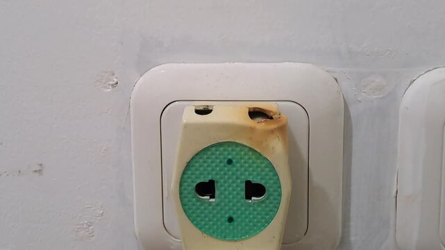 Close-up of a dangerous burnt electric socket adapter plugged into a wall outlet. Electrical hazard, short circuit safety hazard, and risk stock photo.