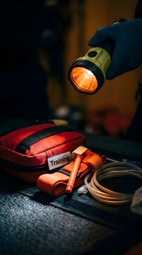 Flashlight gloved hand first aid kit tourniquet medical tubing emergency gear Closeup of gloved hand holding flashlight over first aid kit with tourniquet and medical tubing dark surface