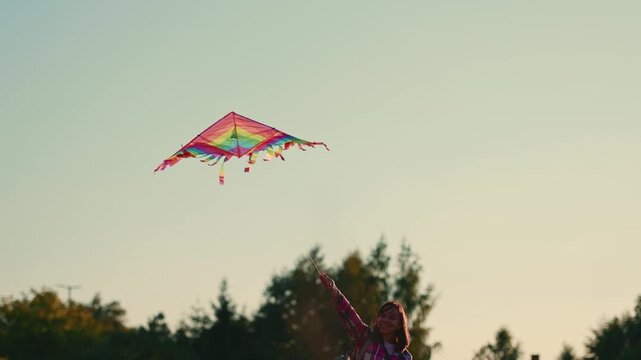 Woman flying a colorful kite in a park as it rises, glides, and dips against the evening sky. Outdoor recreation and carefree summer concept