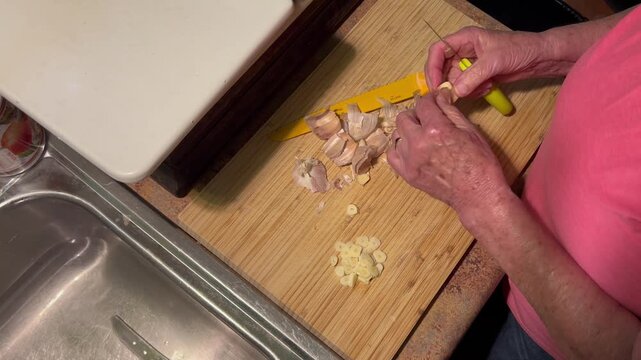 Person peeling garlic cloves on a wooden cutting board in a kitchen