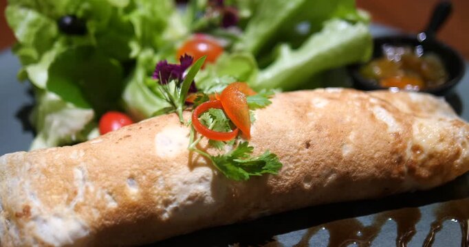 Close up of gourmet burrito wrap crepe roll with fresh vegetable salad in restaurant
