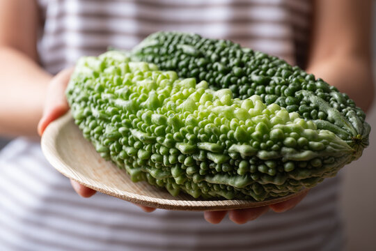 Fresh bitter gourd or bitter melon on a natural plate holding by woman hand, Asian vegetables and herbal medicine