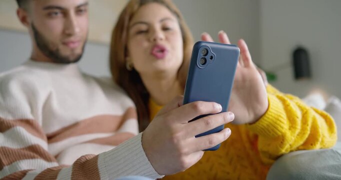 African American couple holding matte blue phone on sofa on call, woman in yellow sweater waving