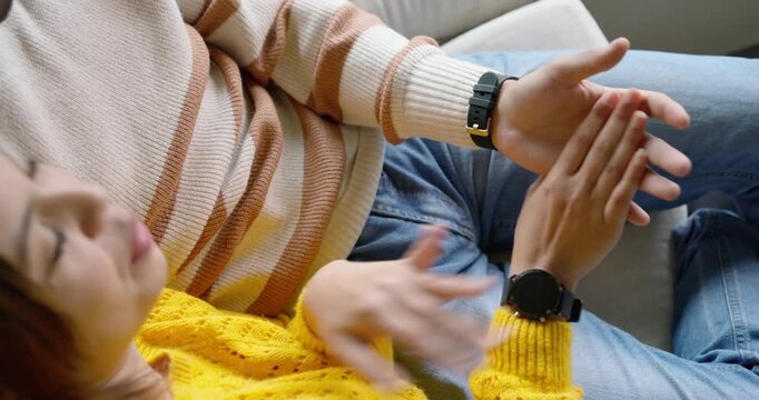 African American couple sitting on sofa, woman reaching toward man's hands, tapping watch playfully