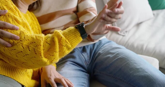African couple sitting on sofa reaching interlacing showing dark watches smiling in yellow sweater