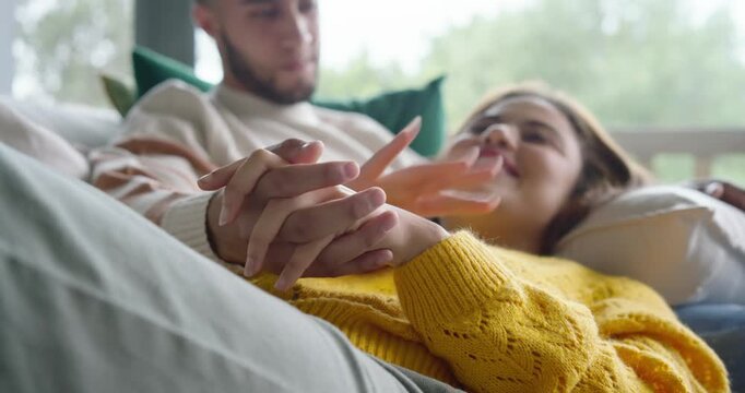 Couple reclining on sofa, woman in yellow sweater while man reaching, massaging hands, showing love