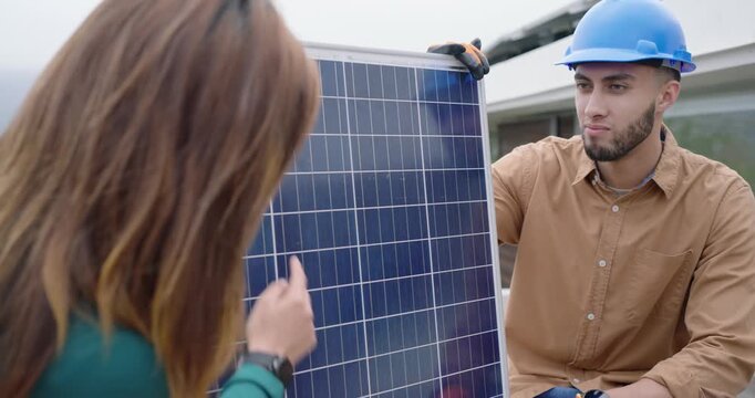 Installer using clamp and gloves placing solar panel on roof deck, homeowner inspecting placement