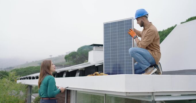 Male tech placing, aligning, securing solar panel on flat roof, female rep using tablet, copy space
