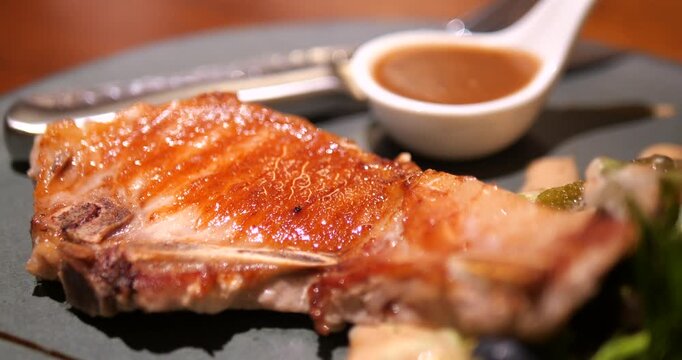 Close up of grilled juicy pork chop steak with brown gravy sauce in restaurant