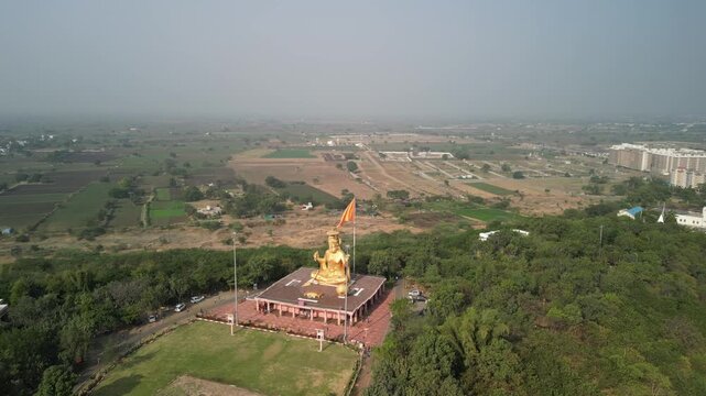 Golden Hanuman statue surrounded by green trees at Pitreshwar Dham