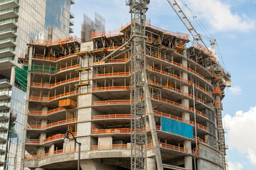 Unfinished concrete framework of a high-rise building construction site with a tall metal tower crane and protective orange safety netting. © AncientAftertone