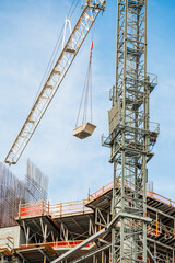 Heavy metal container suspended by steel chains from a long crane boom operating above an unfinished concrete building framework with rebar. © AncientAftertone