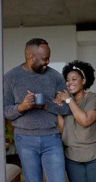 Vertical video: African American couple by doorway man holding mug as woman linking arm in love