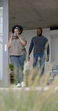Vertical video: African American couple walking on porch woman drinking coffee man touching her arm