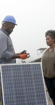 Vertical video: African tech in hard hat checking cable after client pointing at roof for panel fix