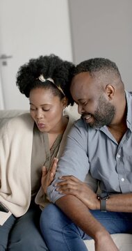 Vertical video: African couple watching phone, seeing clip, touching and laughing on sofa