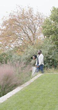 Vertical video: African couple entering via fence walking down stone edge beside lawn admiring view